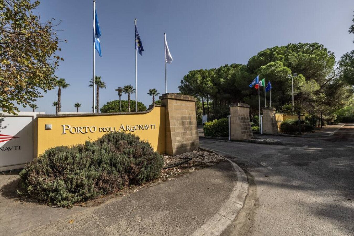 A building entrance with a sign reading 'Porto degli Argonauti' and multiple flags.