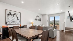 A modern living room with a wooden dining table, grey sofa, and a mountain landscape mural on the wall. - Snowbasin Chalet R5061 |Ski Escape|Firepit |Hot Tub (Mountain Green)