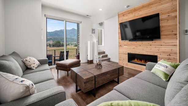 A modern living room with a large TV, fireplace, and a view of mountains through the sliding glass door. - Snowbasin Chalet R5061 |Ski Escape|Firepit |Hot Tub (Mountain Green)