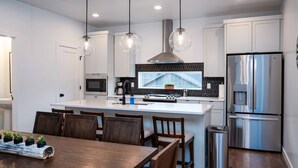 A modern kitchen with white cabinetry, a central island, a stainless steel refrigerator, and pendant lighting. - Snowbasin Chalet R5061 |Ski Escape|Firepit |Hot Tub (Mountain Green)