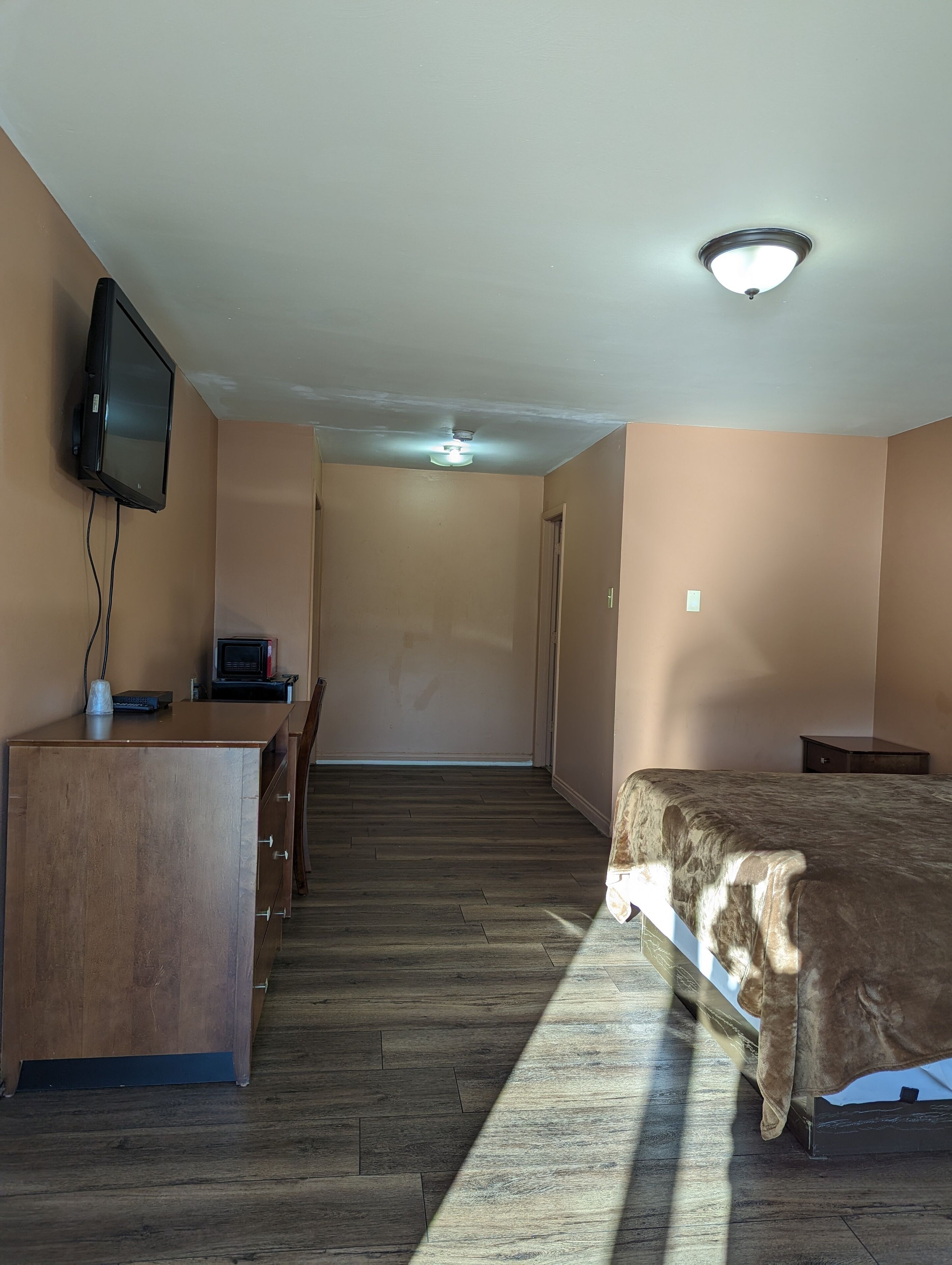 A hotel room with a wooden desk, a bed, and a television mounted on the wall.