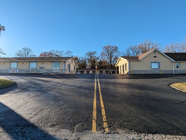 A parking lot with a double yellow line in the center, leading to a row of beige buildings with large windows and a garage door.