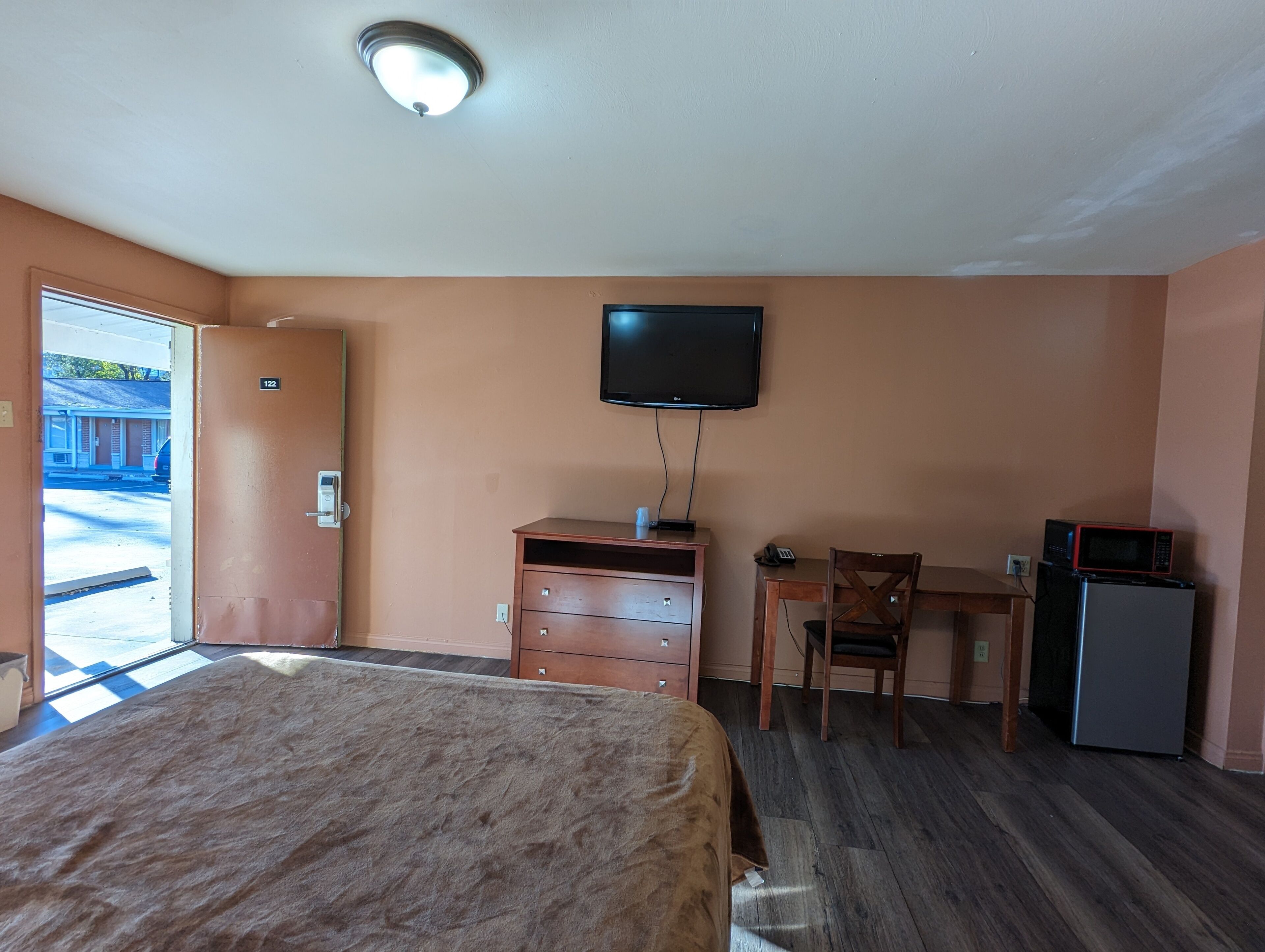 A hotel room with a bed, a desk, a television, and a refrigerator.