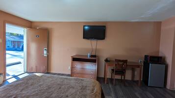 A hotel room with a bed, a desk, a television, and a refrigerator.