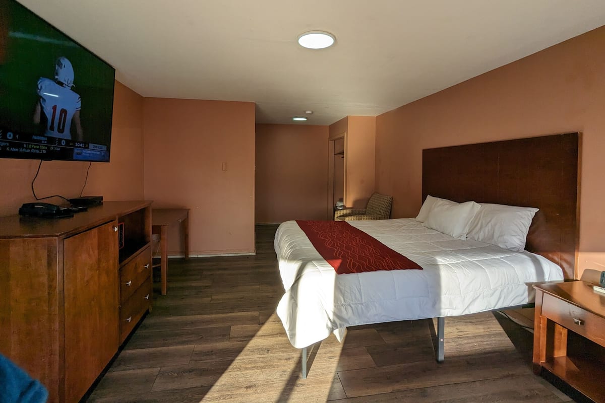 Une chambre d’hôtel avec un lit, un bureau, un téléviseur fixé au mur et une commode en bois.