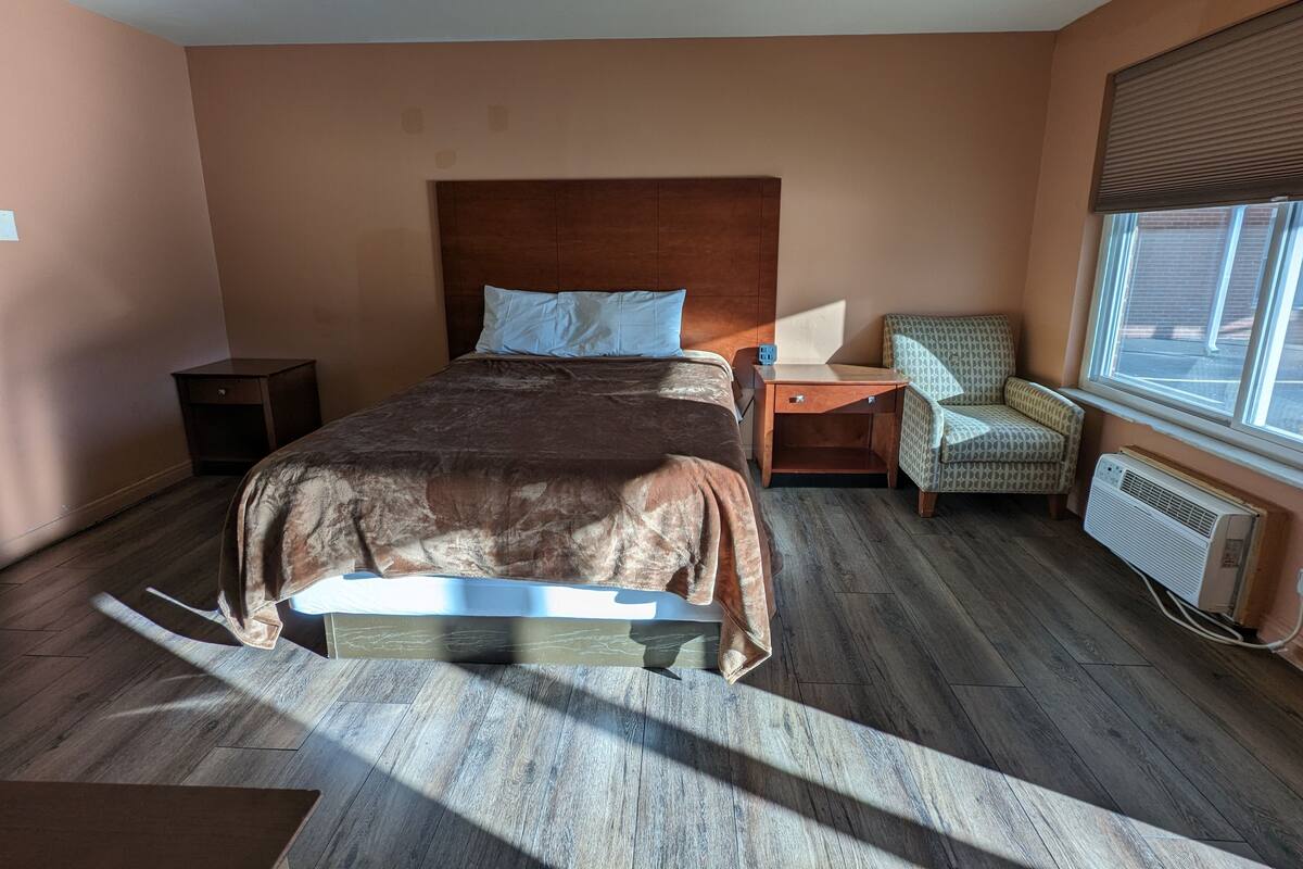 Une chambre à coucher avec un lit, des tables de chevet, une chaise, une fenêtre et un radiateur.