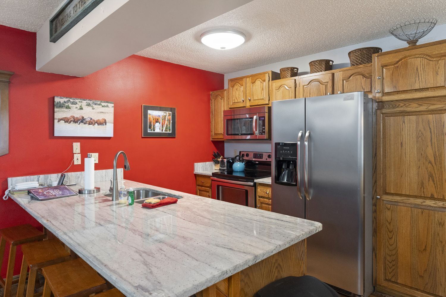 A kitchen with wooden cabinets, a stainless steel refrigerator, a microwave, and a sink.