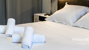 A neatly made bed with white linens and rolled towels, a bedside lamp, and a headboard.