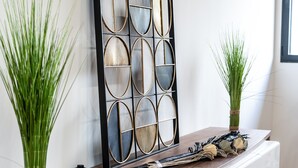 A modern interior with a wooden console table, decorative vases with green plants, a geometric wall art piece, and a stack of magazines.