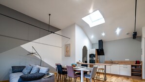 A modern kitchen with a central island, a dining area with a table and chairs, and a loft-style sleeping area with a sofa.