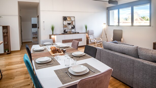 A modern living room with a dining area, a grey sofa, and a dining table set for four.