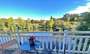 Uma varanda com mesa e cadeiras, com vista para um lago e árvores.