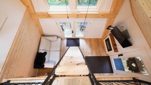 A compact wooden interior with a staircase leading to a loft area, a sofa, and a fireplace. - Peaceful Pines Luxury Treehouse (Lucinda)