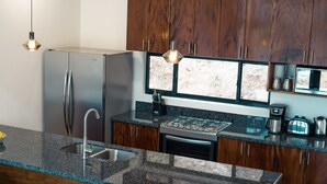 A modern kitchen with granite countertops, stainless steel appliances, wooden cabinets, and pendant lighting. - Enclave Villa V3 -Overlooking Pitons & Ocean ! Wow.  (Soufriere)