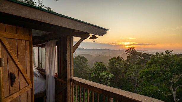 A wooden cabin with a balcony overlooking a forested landscape during sunset. - Alta Sanctuary (Tambopata)