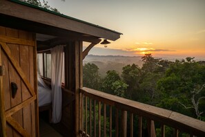 A wooden cabin with a balcony overlooking a forested landscape during sunset. - Alta Sanctuary (Tambopata)