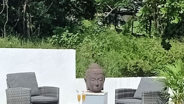A pool area with wicker furniture and a Buddha statue. - Bienvenue à la Maison D'hôtes L'instant Present (Le Moule)