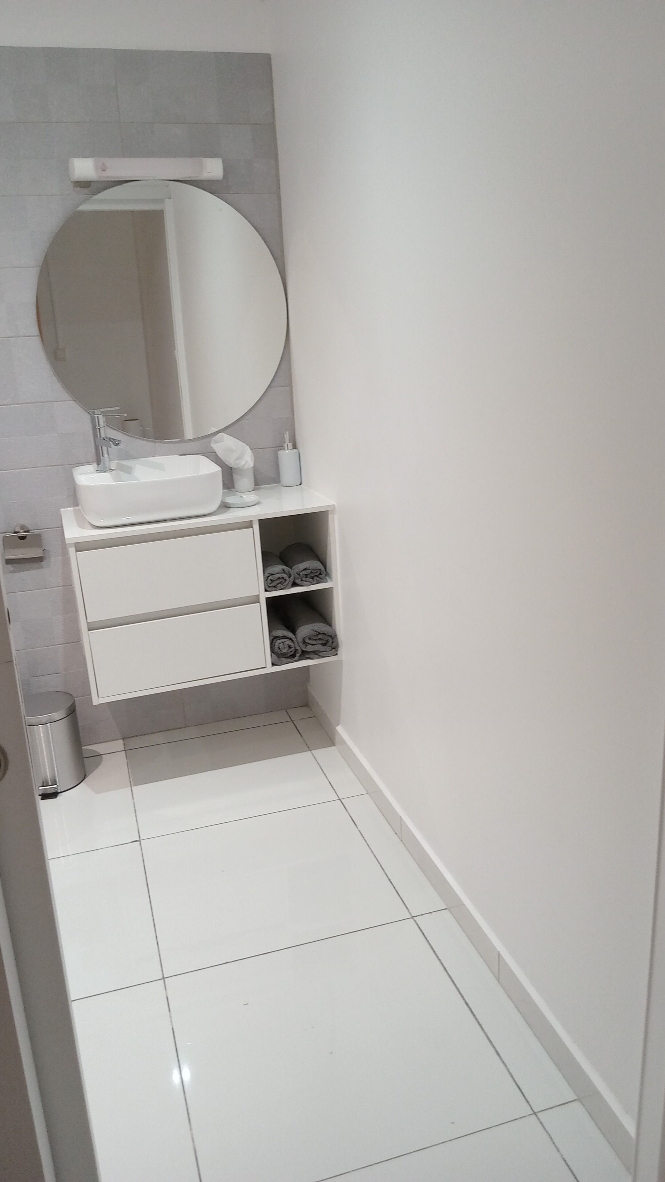 Une salle de bain avec un lavabo blanc, un grand miroir et une étagère avec des serviettes.