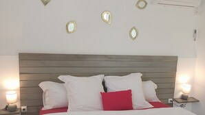 A neatly made bed with white and red pillows, a magazine, and rolled towels. There are wall-mounted mirrors and a ceiling fan. - Bienvenue à la Maison D'hôtes L'instant Present (Le Moule)