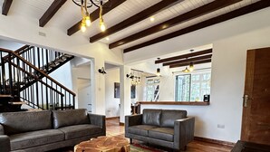 Un salón amplio con suelo de madera, dos sofás grises, una mesa baja de madera y una escalera con barandillas oscuras.