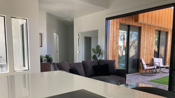 Une cuisine moderne avec un îlot central, un canapé gris et un espace patio aménagé avec des sièges d’extérieur.