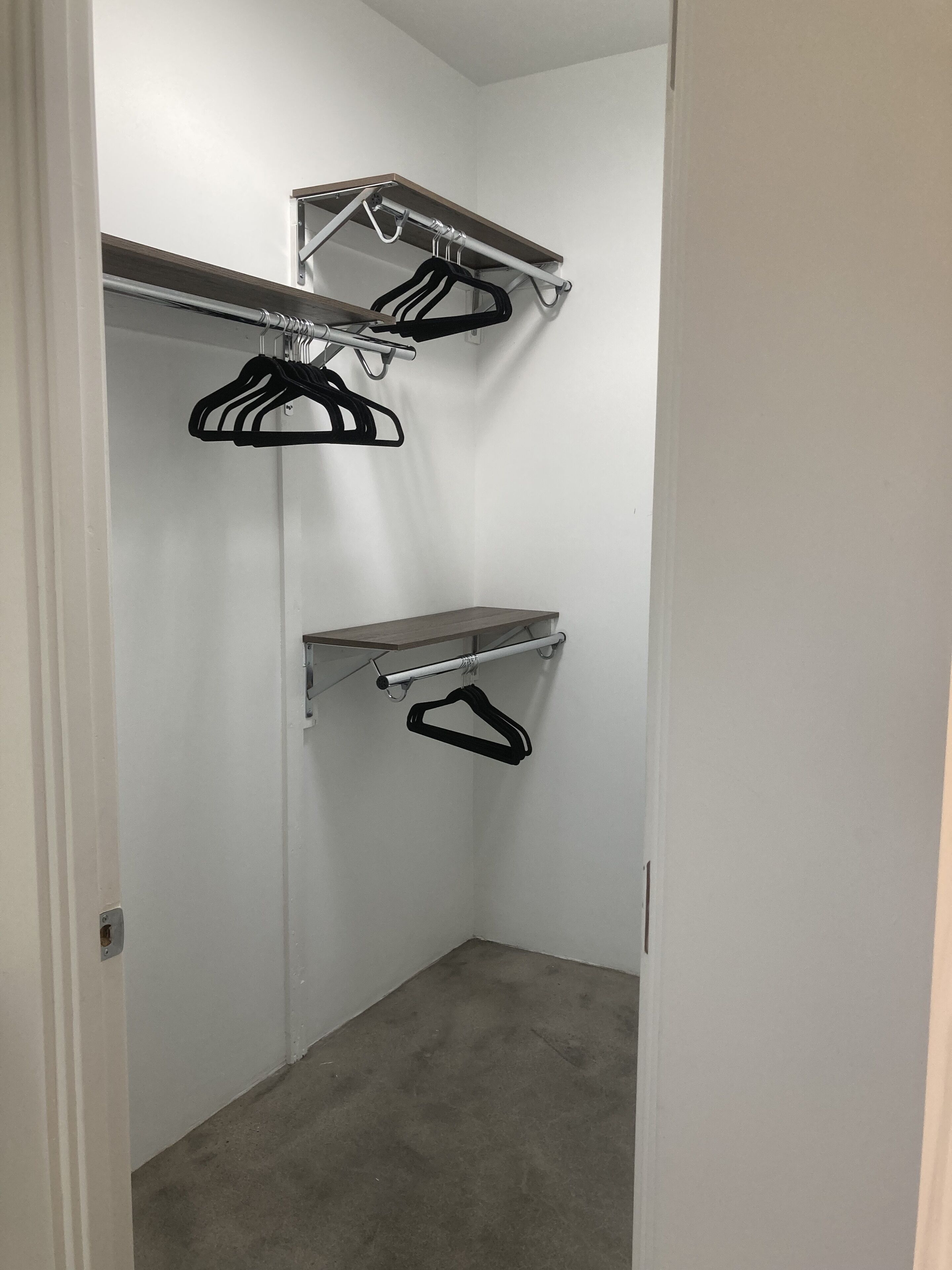 A corner closet with two metal shelves and two black hangers.