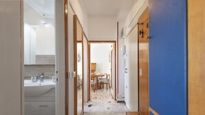 A hallway with a bathroom on the left, a dining area in the center, and a blue door on the right. - GN Milano Navigli - Chic Naviglio Hideaway. (Milano)