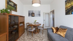 A dining area with a round table, chairs, a cabinet with glass doors, a hanging lamp, and a sofa with cushions. - GN Milano Navigli - Chic Naviglio Hideaway. (Milano)
