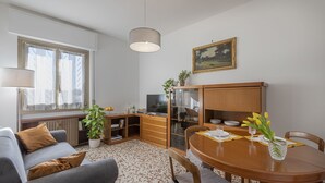 A cozy living room with a sofa, a dining table with chairs, a television, and a bookshelf. - GN Milano Navigli - Chic Naviglio Hideaway. (Milano)
