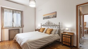 A bedroom with a large bed, wooden floor, a window with sheer curtains, a bedside table with a lamp, and a painting on the wall. - GN Milano Navigli - Chic Naviglio Hideaway. (Milano)