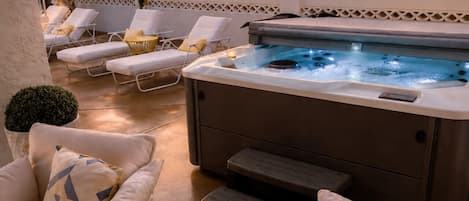 A hot tub with lounge chairs and a small table with a plant, set against a sunset backdrop.