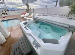 A hot tub with a control panel, a pool, and lounge chairs.