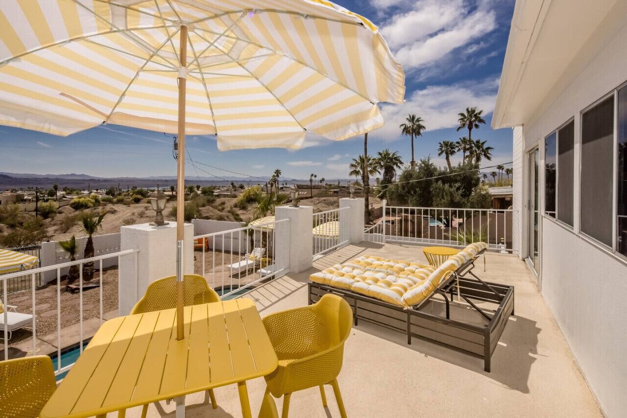 Ein Balkon mit gelben Stühlen, einem gestreiften Sonnenschirm und einem Pool.