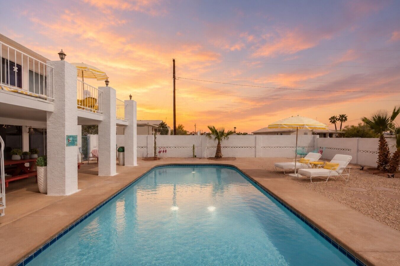 Una piscina con recinzione bianca, sedie a sdraio e cielo al tramonto.