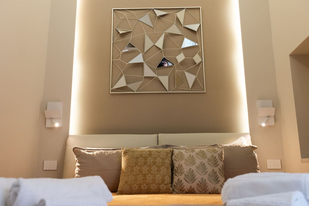 Habitación de hotel con cama, detalles decorativos en la pared y lámparas fijadas a la pared.