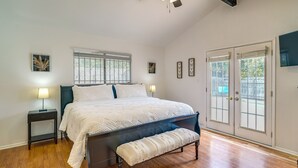 A bedroom with a large bed, a bench, a nightstand, and a window with blinds.