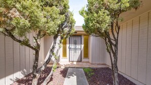 A pathway leading to a gated entrance with a door, flanked by trees and a beige wall.