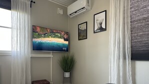 A modern living room with a flat-screen TV, a grey sofa, a white table, and a potted plant. - Modern Cabin (Västra Götalands län)