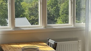 A dining area with a table and chairs, a window with a view of a forest, and a radiator. - Modern Cabin (Västra Götalands län)