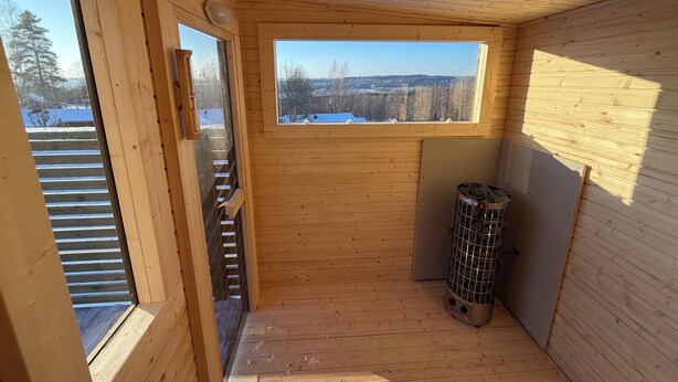 A wooden interior with a window view, a radiator, and a trash bin. - Modern Cabin (Västra Götalands län)