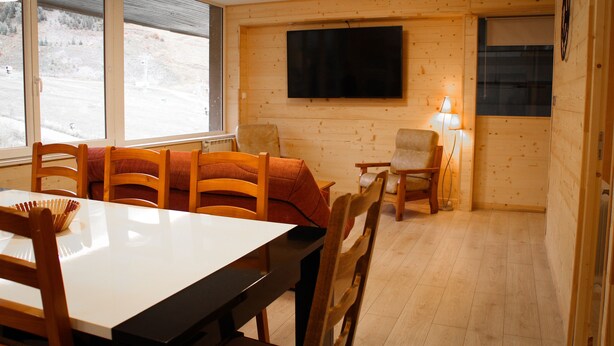 A dining area with a table and chairs, a television mounted on the wall, and a window with a view of a snowy landscape. - L'écrin, Appartement aux Pieds des Pistes (Orcières)