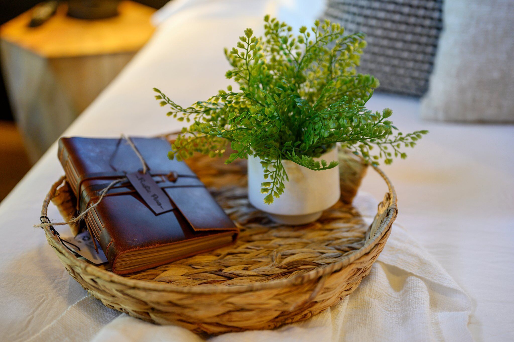 A wicker basket containing a small potted plant and a leather-bound book on a white tablecloth.