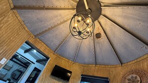Una habitación con techo alto, lámpara central, televisión y ventana con persianas.