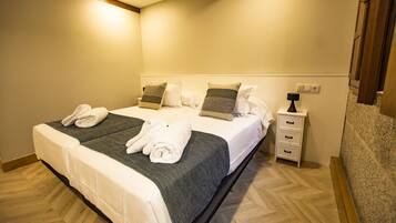 Una cama doble con dos juegos de toallas, una mesita de noche con lámpara y un mueble auxiliar con cajones.