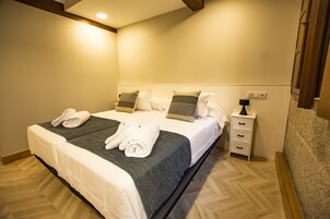 Una cama doble con dos juegos de toallas, una mesita de noche con lámpara y un mueble auxiliar con cajones.