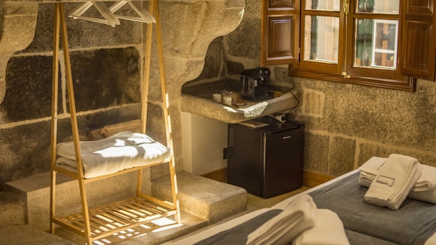 A stone-walled room with a bed, a small sink, and a window with wooden shutters. - NÓMADE SANTIAGO (Santiago de Compostela)