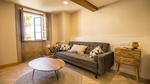 A living room with a grey sofa, a round coffee table, a wooden side table, and a window with curtains. - NÓMADE SANTIAGO (Santiago de Compostela)