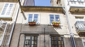 A stone building with two windows, each with a flower box. There is a sign above the door that reads "NOMADE HOSTAL". - NÓMADE SANTIAGO (Santiago de Compostela)