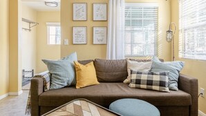 A living room with a brown sofa, multiple cushions, a patterned rug, and framed artwork on the wall.
