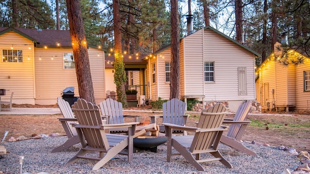 A cabin with a fire pit and Adirondack chairs in the yard.